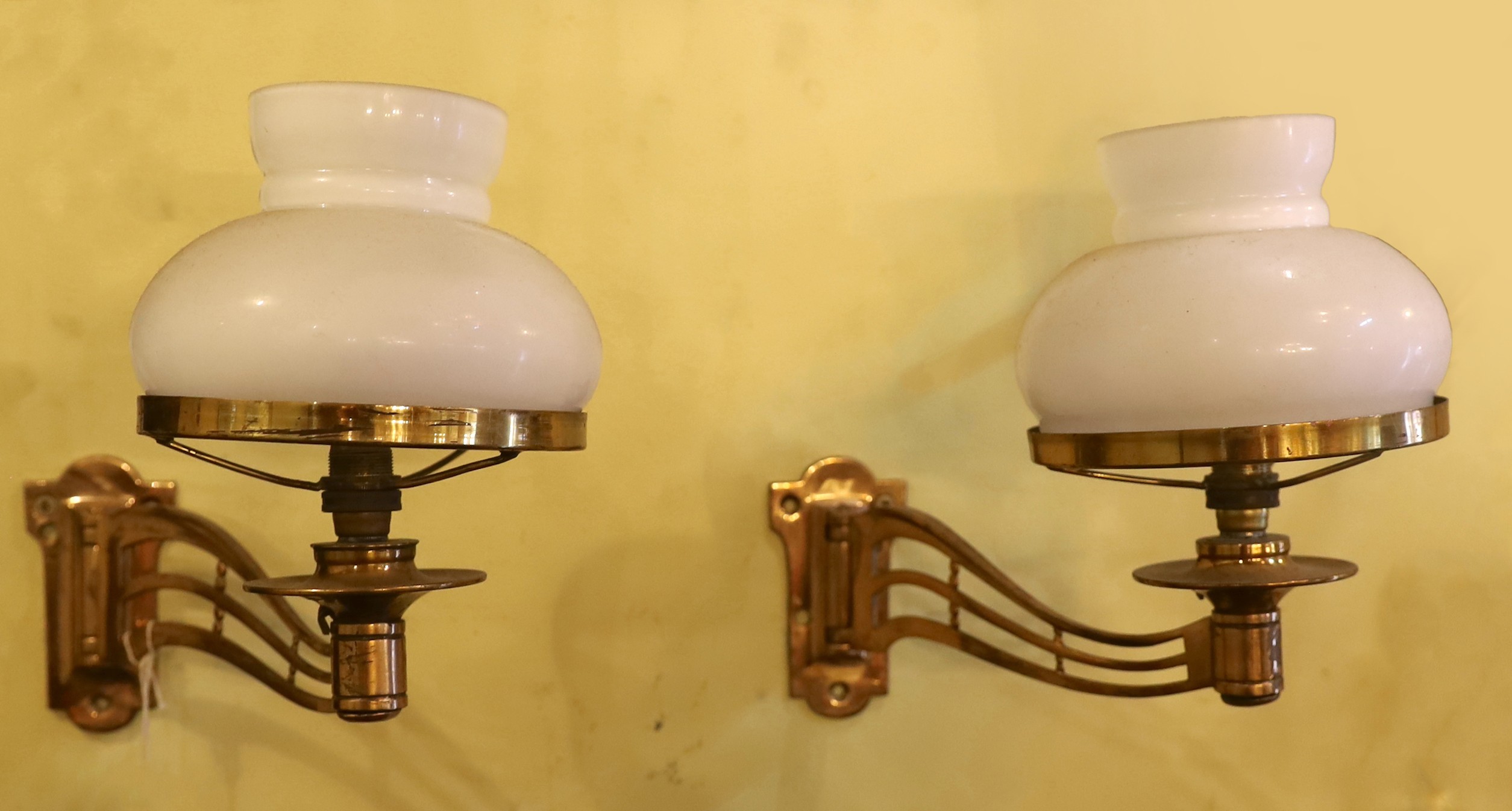 A pair of late Victorian brass swivelling wall lights with opaque glass shades, height 25cm. depth 25cm